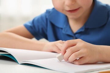 Little boy erasing mistake in his notebook at white desk, closeup