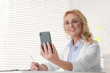 Doctor with glasses and smartphone consulting patient in clinic. Online medicine concept