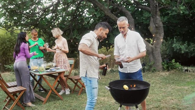 Two men adult friends cooking barbecue and drinking beer preparing garden meal
