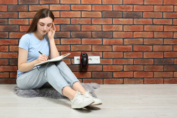 Woman sitting on floor while charging electric heater indoors, space for text