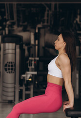 a beautiful girl in the gym sits on a bench