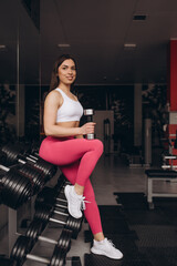 Fit young woman sitting and resting after workout or exercise in fitness gym.