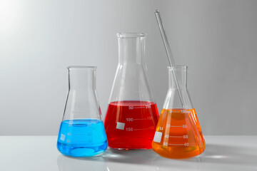 Glass flasks with colorful liquids on white table against grey background