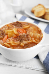 Tasty cabbage soup with meat and carrot on white wooden table, closeup