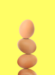 Stacked fresh chicken eggs against light yellow background