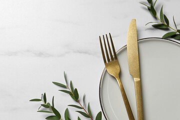 Stylish setting with cutlery and eucalyptus leaves on white marble table, flat lay. Space for text