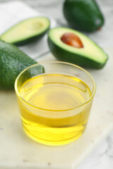 Bowl with oil and fresh avocados on white marble table, closeup