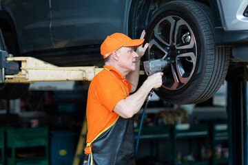 Professional car mechanic changing car wheel at Car maintenance and auto service garage. Caucasian man worker people
