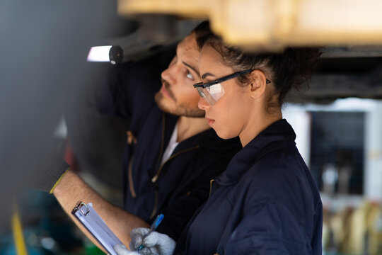 Hispanic Female trainee Mechanics Working Underneath Car Together Car maintenance and auto service garage. Car maintenance and auto service garage concept.