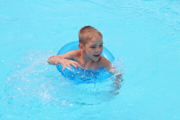 Funny little boy swims in a pool in an blue ring top view