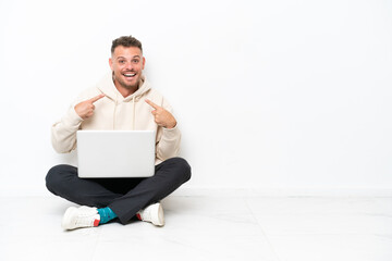 Young caucasian man with a laptop sitting on the floor isolated on white background with surprise facial expression