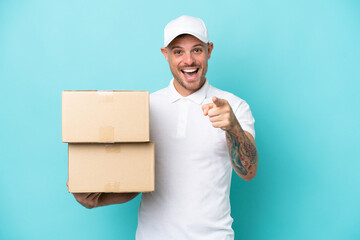 Delivery caucasian man isolated on blue background surprised and pointing front