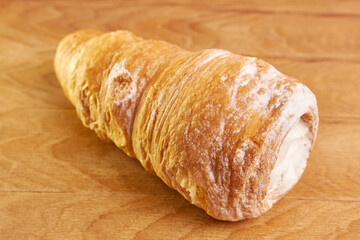 A pipe of puff pastry with cream on a wooden background.