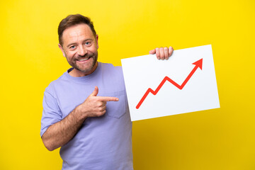 Middle age caucasian man isolated on yellow background holding a sign with a growing statistics arrow symbol and  pointing it