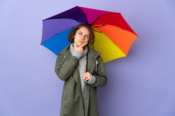 English woman holding an umbrella isolated on purple background having doubts