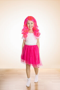 Little girl smiling at camera wearing pink skirt and pink hair wig.