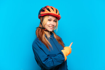 Young cyclist girl isolated on blue background pointing back