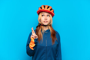 Young cyclist girl isolated on blue background with fingers crossing and wishing the best