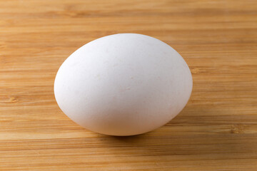 Whole white chicken egg on a wooden surface side lit