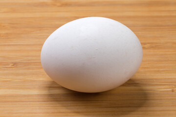 Whole white chicken egg illuminated from above on wooden surface