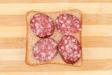 Open sandwich with dry-cured sausage on bamboo cutting board