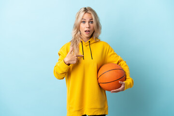 Young Russian woman playing basketball isolated on blue background with surprise facial expression