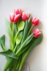 green fork and spoon with tulips on a plain light background