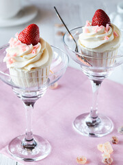 two cupcakes with white cream and strawberries in glasses on a light wooden table