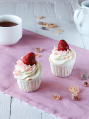 two cupcakes with white cream and strawberries on a light wooden table