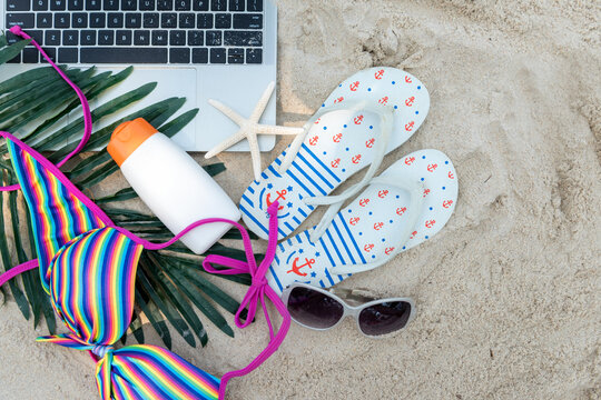 Summer Travel.  Top view laptop of tourism freelance working and vacation summer on the beach with sunblock and sandals.  Summer trip holiday