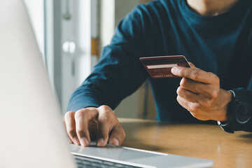 Man hand holding credit card and using laptop at home, Businessman or entrepreneur working, Online shopping, e-commerce, internet banking, spending money concept.