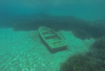 An old rowing boat is abandoned on the sandy bottom under the water.