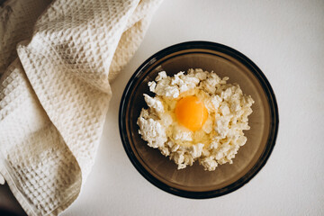 cottage cheese, egg and salt in a black glass bowl on a white table. light towel on the table. making breakfast with your own hands
