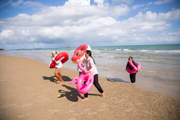 Happy retiredment life. Group of elderly Asian man and woman friends running with Bright inflatable ring to the beach.