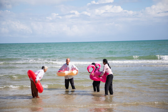 Happy retiredment life. Group of elderly Asian man and woman friends running with Bright inflatable ring to the beach.
