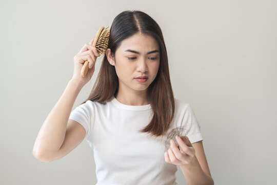 Serious asian young woman holding brush holding comb, hairbrush with fall black hair from scalp after brushing, looking on hand worry about balding. Health care, beauty treatment, hair loss problem.