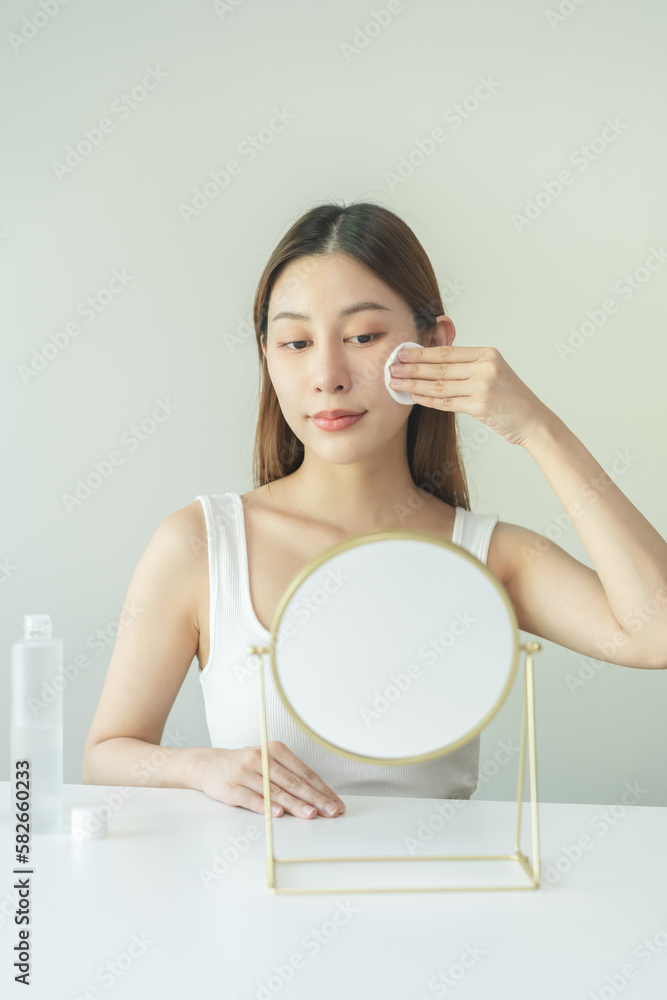 Wall mural Happy beauty, attractive asian young woman, girl looking reflect in mirror, hand holding cotton pad, applying facial wipe on her face remover makeup, essence or lotion for treatment, skin care routine