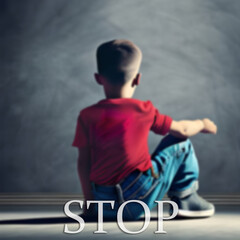 A boy sitting on the floor in front of a blackboard that says stop.