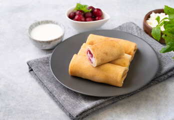 Homemade crepes with chery berry and a cottage cheese on a plate on a blue background with sour cream.