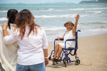 Fototapeta na wymiar Happy holidays with family. Travel and vacations concept. Happy Asian family and woman elderly handicap on wheelchair walking together on the beach.