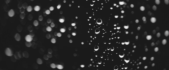 Atmospheric minimal grayscale backdrop with rain droplets on glass. Wet window with rainy drops and dirt spots closeup. Blurry minimalist monochrome background of dirty window glass with raindrops.