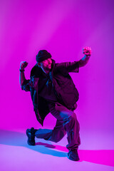 Fototapeta na wymiar Fashionable professional dancer man in stylish urban clothes dancing in a creative color studio with pink and neon lights