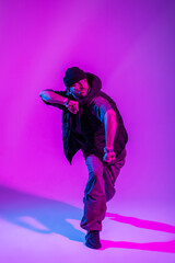 Stylish professional dancer man in trendy clothes dancing in color studio with pink and blue light