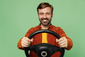 Elderly smiling happy fun cool man 40s years old he wears casual clothes red shirt t-shirt hold steering wheel driving car look camera isolated on plain pastel light green background studio portrait.