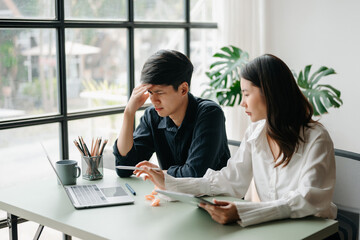 Fototapeta premium Two Asian people feeling migraine head strain.Overworked businesswoman financier while working on laptop and tablet at home office.