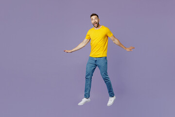 Fototapeta na wymiar Full body young excited surprised caucasian man wear yellow t-shirt jump high with outstretched hands look camera isolated on plain pastel light purple background studio portrait. Lifestyle concept.