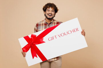 Big young surprised Indian man wearing brown shirt casual clothes hold gift certificate coupon...