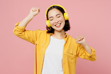 Young happy cheerful fun woman of Asian ethnicity wears yellow shirt white t-shirt headphones...