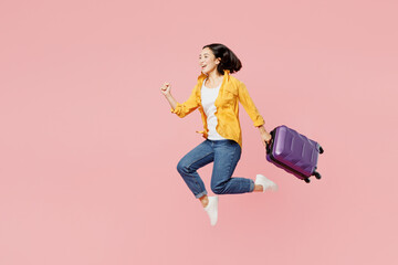 Side view traveler woman wear casual clothes hold suitcase bag jump high isolated on plain pastel pink background Tourist travel abroad in free spare time rest getaway Air flight trip journey concept - obrazy, fototapety, plakaty