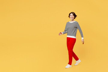 Fototapeta na wymiar Full body smiling happy fun cheerful cool young woman wear casual black and white shirt walking going strolling look camera isolated on plain yellow color background studio portrait. Lifestyle concept